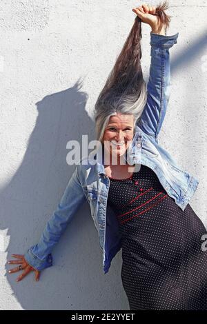 Una donna più anziana che ride allunga i suoi lunghi capelli grigi verso l'alto Foto Stock