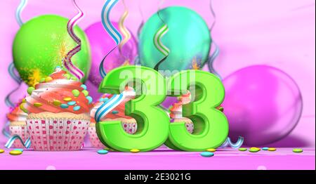 Cupcake di compleanno con candela di accensione con il numero 33 grande in verde con cupcake con crema rossa decorata con cioccolato fiches e palloncini sul th Foto Stock
