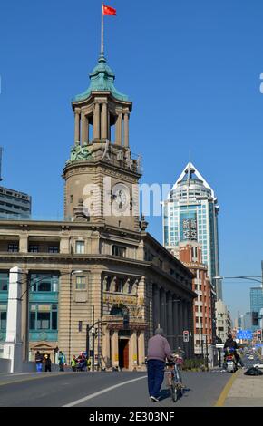 Un anziano gentiluomo spinge la sua bicicletta sul ponte di Waaibaidu a Shanghai, interessante torre di orologio sullo sfondo. Foto Stock