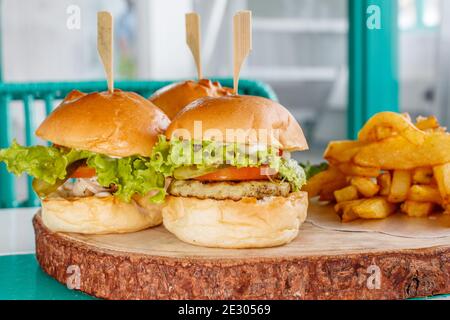 Tre cursori di pesce (mini hamburger) con lattuga, pomodoro e sottaceti, serviti con patatine fritte su un vassoio di legno Foto Stock