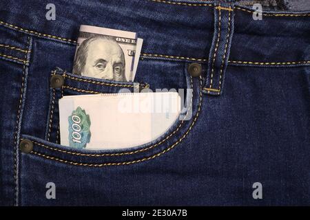 Un pacchetto di dollari americani e rubli russi in una tasca di jeans blu. Denaro in contanti. Foto Stock
