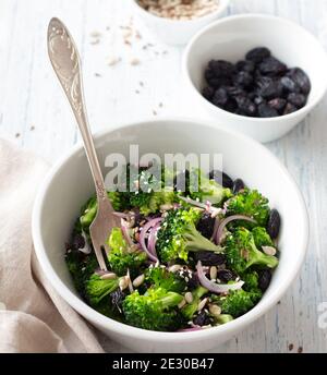 Insalata fresca con broccoli, uva passa nera, cipolle rosse, semi, sesamo e lino su sfondo leggero. Cibo salutare. Concentrazione selettiva Foto Stock