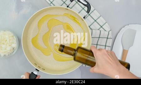 Lo chef versa l'olio d'oliva dalla bottiglia in una padella, avvicina il processo di cottura e guarda dall'alto Foto Stock