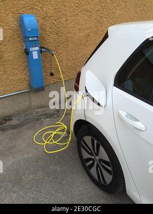 Stoccolma, Svezia - 09 aprile 2015: Primo piano della ricarica di auto elettriche moderne europee per strada, veicolo bianco accanto a un caricabatteria blu per auto pubbliche Foto Stock