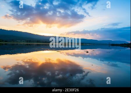 Un lago tranquillo sul tramonto estivo, le nuvole drammatiche e il tramonto riflessi del cielo sul lago, le montagne sullo sfondo. Parco Nazionale di Khao Yai, Tailandia. Foto Stock