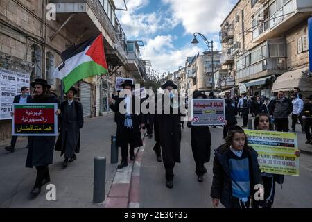 I membri di Neturei Karta, un movimento ebreo ultra-ortodosso frangia all'interno del blocco anti-sionista portano la bandiera palestinese e gridano slogan mentre camminano attraverso il quartiere religioso di Mea Shearim il 14 gennaio 2021, a Gerusalemme, Israele. Neturei Karta si oppone al sionismo e chiede uno 'smantellamento pacifico' dello Stato d'Israele, nella convinzione che agli ebrei è vietato avere il proprio stato fino all'avvento del Messia ebraico e che lo stato d'Israele è una ribellione contro Dio. Foto Stock