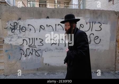 Un ebreo ultra ortodosso passa accanto a un muro con graffiti anti-sionismo odio spruzzati da ebrei estremisti anti-sionisti Haredi nel quartiere ultra ortodosso di Mea Shearim a Gerusalemme Ovest Israele. Neturei Karta si oppone al sionismo e chiede uno "smantellamento pacifico" dello Stato di Israele, nella convinzione che agli ebrei sia proibito avere il proprio stato fino alla venuta del Messia ebraico e che lo Stato di Israele sia una ribellione contro Dio. Foto Stock