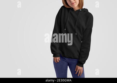 Serie di abiti mockup. Bella donna gracile in una felpa con cappuccio nera e pantaloni blu isolato sullo studio vuoto backgrounds.Frontal posa. Il modello può utilizzare i Foto Stock