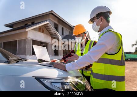 Architetto e supervisori che utilizzano un computer portatile nel cantiere, idee di costruzione della casa durante l'epidemia di coronavirus. Foto Stock