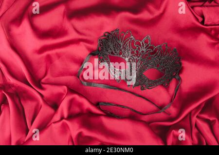 Maschera veneziana nera con luccicanti tessuti di seta rossa Foto Stock