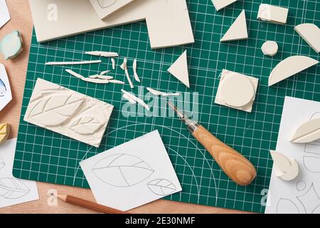 Scalpello a testa e matita posizionati vicino a schizzi e gomma per incisione con timbro sulla scrivania in officina Foto Stock