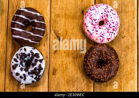 Ciambelle colorate su un tavolo in legno. Zucchero dolce glassa alimentare con spruzzette glassate, ciambella con glassa di cioccolato. Vista dall'alto con spazio di copia Foto Stock