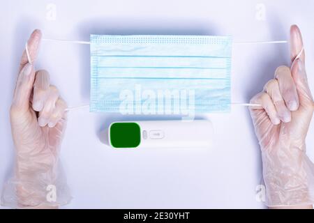 Termometro senza contatto, guanti e maschera medica su sfondo bianco. Foto Stock