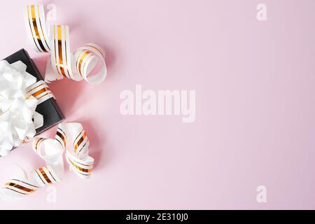 Confezione regalo avvolta in nastro a righe bianche e dorate su sfondo rosa pastello. Nota vuota legata. Spazio di copia Foto Stock