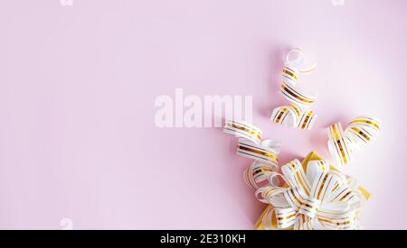 Confezione regalo avvolta in nastro a righe bianche e dorate su sfondo rosa pastello. Nota vuota legata. Spazio di copia Foto Stock