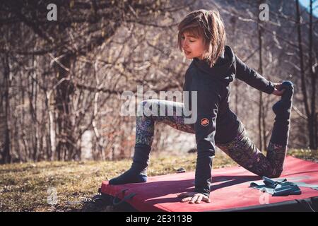 Una donna fa yoga su un tappeto di bouldering all'aperto dentro il sole Foto Stock