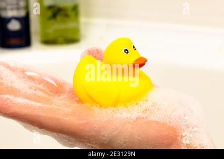 giocattolo giallo brillante che anatroccolo a portata di mano in bagno uno sfondo chiaro Foto Stock