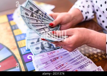 Gioco finanziario a bordo domestico durante la quarantena. Una donna tiene in mano un pacchetto di dollari ed euro vinti in un gioco da tavolo. Formazione delle competenze aziendali Foto Stock