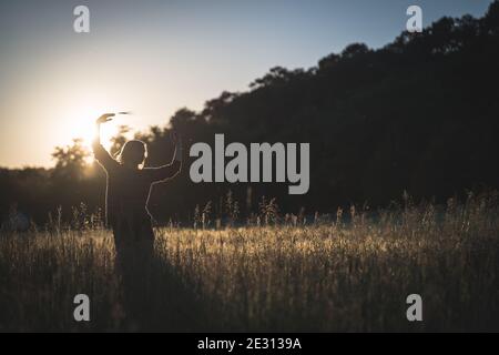 Una giovane donna danzava nell'erba alta, retroilluminata dal sole che tramonta durante l'ora d'oro Foto Stock