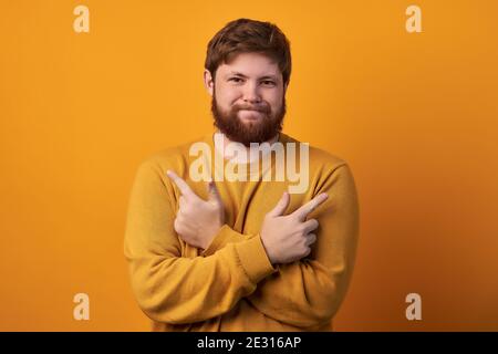 Perplesso incerto l'uomo europeo attraversa le mani e i punti lateralmente, sceglie tra due oggetti, dovrebbe decidere, affronta scelta complicata, indica andare Foto Stock