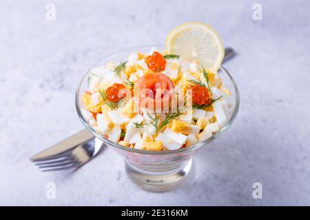 Insalata a strati con trota salata (salmone), caviale, uova e verdure. Piatto tradizionale, una porzione in calice di vetro su sfondo grigio. Primo piano. Foto Stock