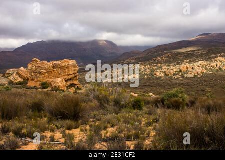 I massi di arenaria delle montagne di Cederberg, sudafricane, dagli agenti atmosferici e spazzati dal vento, con luce che si infrangono attraverso le nubi della tempesta che si radunano Foto Stock