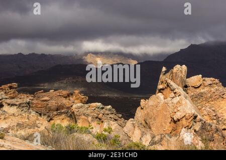 I massi di arenaria delle montagne di Cederberg, sudafricane, dagli agenti atmosferici e spazzati dal vento, con luce che si infrangono attraverso le nubi della tempesta che si radunano Foto Stock