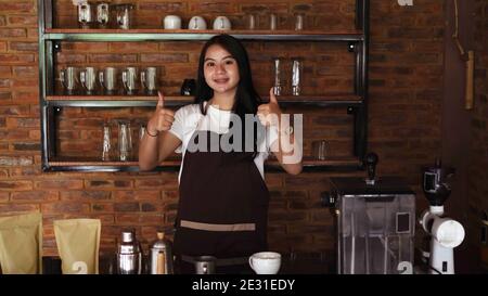 Giovane donna asiatica barista indossare grembiule OK gesto Foto Stock