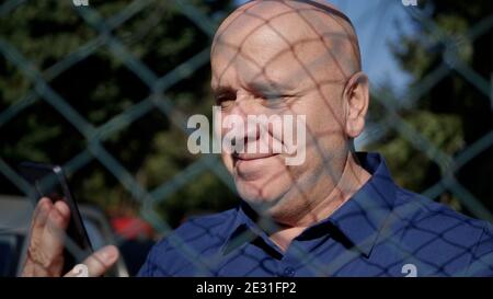 Immagine con una persona anziana dietro una recinzione metallica utilizzando Uno smartphone Foto Stock