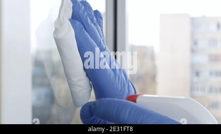 Immagine con le mani indossare guanti protettivi pulire una finestra usando Liquido disinfettante spruzzato Foto Stock