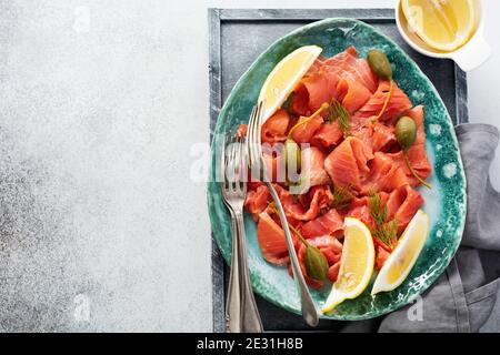 Fette di salmone leggermente salato con capperi, limone e aneto su un piatto di ceramica su fondo grigio di cemento. Vista dall'alto. Foto Stock