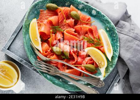 Fette di salmone leggermente salato con capperi, limone e aneto su un piatto di ceramica su fondo grigio di cemento. Vista dall'alto. Foto Stock