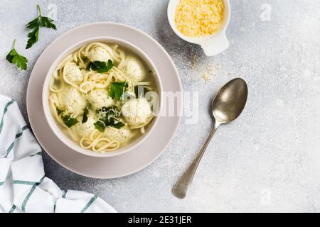 Zuppa con polpette di pollo e pasta d'uovo, parmigiano, prezzemolo in un recipiente in ceramica su uno sfondo grigio. Brodo italiano tradizionale. Vista dall'alto. Foto Stock