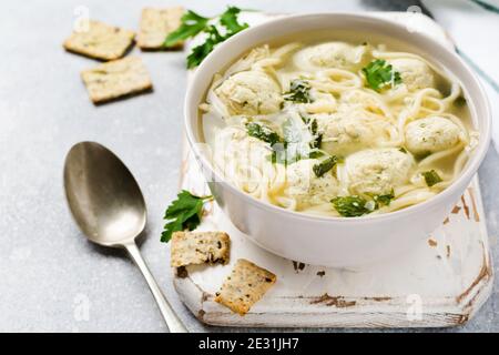 Zuppa con polpette di pollo e pasta d'uovo, parmigiano, prezzemolo in un recipiente in ceramica su uno sfondo grigio. Brodo italiano tradizionale. Vista dall'alto. Foto Stock