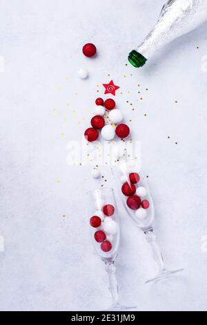 Due bicchieri per champagne e una bottiglia di champagne di Natale con spruzzette Sotto forma di albero di Natale fatto di rosso e. palline bianche di giocattoli decorate golde Foto Stock