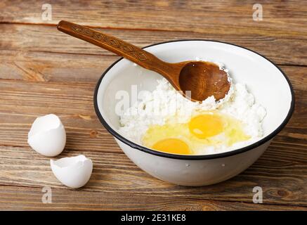 Ciotola con il formaggio e le uova su marrone tavolo in legno. Cucchiaio di legno in una ciotola. Ingredienti per il cheesecake fatti in casa o la cottura. Foto Stock