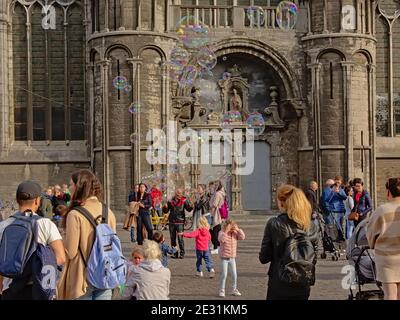 Artista di strada circondato dal pubblico, facendo grandi bolle di corda di fronte alla chiesa medievale di San Nicola a Gand, Belgio Foto Stock