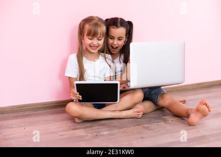 Stupite bambine che mostrano una t-shirt bianca, isolate su sfondo rosa. Concetto di stile di vita infantile. Spazio di copia fittizio. Punta del dito indice Foto Stock