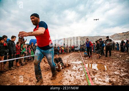 Idlib, Siria. 16 gennaio 2021. Un attivista tira un bambino nel fango al campo di Baraem Abu al Feda durante un evento di intrattenimento. Attivisti nella campagna dell'Idlib hanno organizzato un evento di intrattenimento per portare gioia ai bambini e dimenticare le loro sofferenze, le attività si sono svolte nel campo di Baraem Abu al Feda, a ovest della città di 'armada'. Le attività includono il calcio, la pittura e il gioco nel fango. Credit: SOPA Images Limited/Alamy Live News Foto Stock