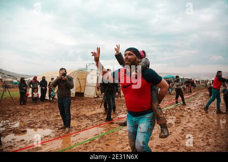 Idlib, Siria. 16 gennaio 2021. Un attivista porta un bambino sulle spalle al campo di Baraem Abu al Feda durante un evento di intrattenimento. Attivisti nella campagna dell'Idlib hanno organizzato un evento di intrattenimento per portare gioia ai bambini e dimenticare le loro sofferenze, le attività si sono svolte nel campo di Baraem Abu al Feda, a ovest della città di 'armada'. Le attività includono il calcio, la pittura e il gioco nel fango. Credit: SOPA Images Limited/Alamy Live News Foto Stock