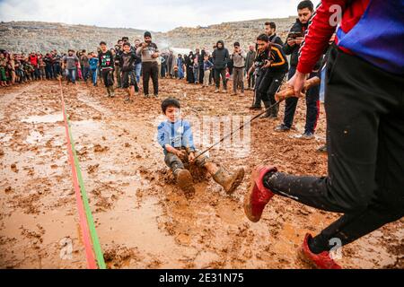 Idlib, Siria. 16 gennaio 2021. Un attivista tira un bambino nel fango al campo di Baraem Abu al Feda durante un evento di intrattenimento. Attivisti nella campagna dell'Idlib hanno organizzato un evento di intrattenimento per portare gioia ai bambini e dimenticare le loro sofferenze, le attività si sono svolte nel campo di Baraem Abu al Feda, a ovest della città di 'armada'. Le attività includono il calcio, la pittura e il gioco nel fango. Credit: SOPA Images Limited/Alamy Live News Foto Stock