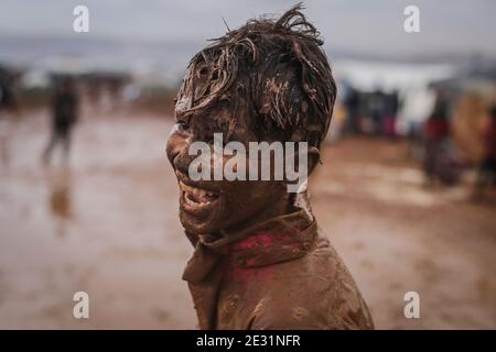 Sarmada, Siria. 16 gennaio 2021. Un ragazzo siriano coperto di sorrisi di fango durante una competizione sportiva organizzata da volontari nel campo di Baraem per sfollati interni. Credit: ANAS Alkharboutli/dpa/Alamy Live News Foto Stock