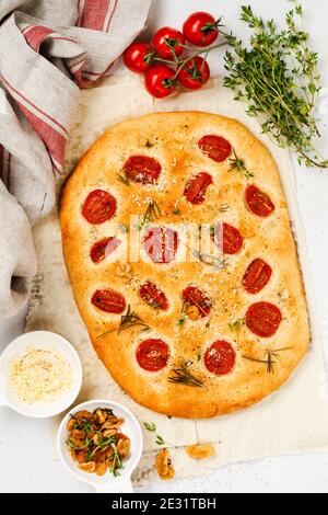 Focaccia tradizionale italiana con pomodori ciliegini, parmigiano e rosmarino su sfondo marrone chiaro. Vista dall'alto. Foto Stock