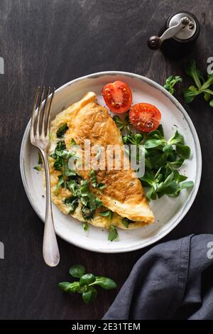 Omelette ripiena con pomodori, peperone rosso, formaggio cremoso e mais o lattuga di agnello su sfondo di legno scuro con spazio per la copia. Alimentazione sana Foto Stock