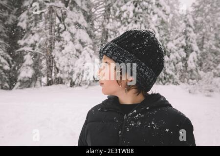 Young Boy si alza di profilo con fiocchi di neve attaccati al suo Beanie. Foto Stock