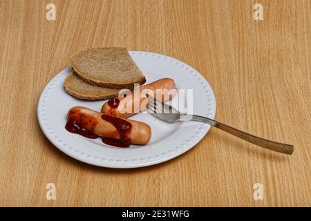 Due salsicce, pane e forchetta sul piatto bianco Foto Stock