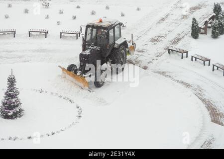 il trattore-escavatore rimuove la neve nel cortile della città. lavoro di servizi pubblici Foto Stock