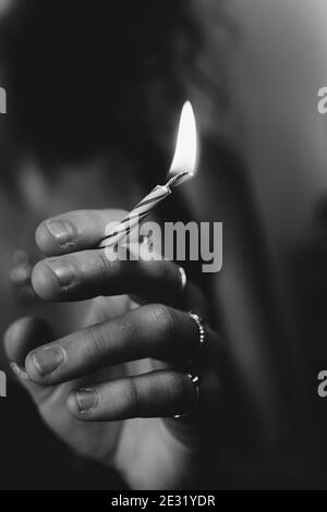 Scala di grigi fuoco superficiale di una mano femmina che tiene un candela di compleanno illuminata come sigaretta Foto Stock