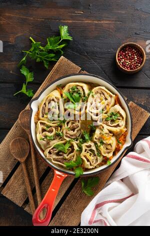 Involtini di pasta di carne con carne o 'gnocchi pigri' in una padella di ghisa su un vecchio fondo rustico di legno. Vista dall'alto. Foto Stock