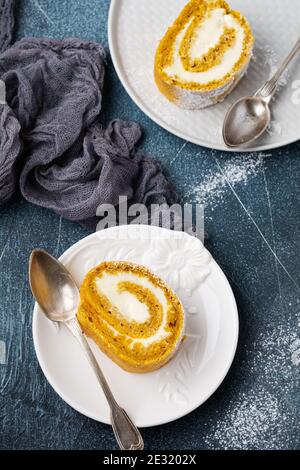 Rotolo di zucca da dessert con crema al burro e arancio su fondo di cemento blu scuro. Messa a fuoco selettiva. Foto Stock